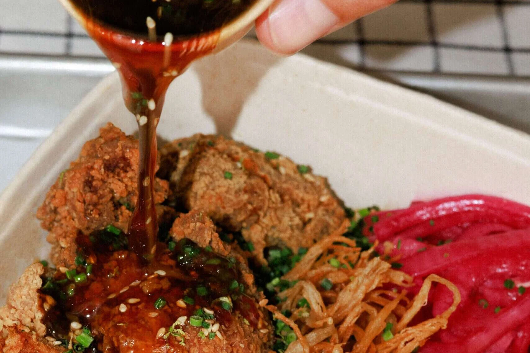 Sauce being poured over a karaage chicken rice bowl at Wishbone in Bica, Lisbon